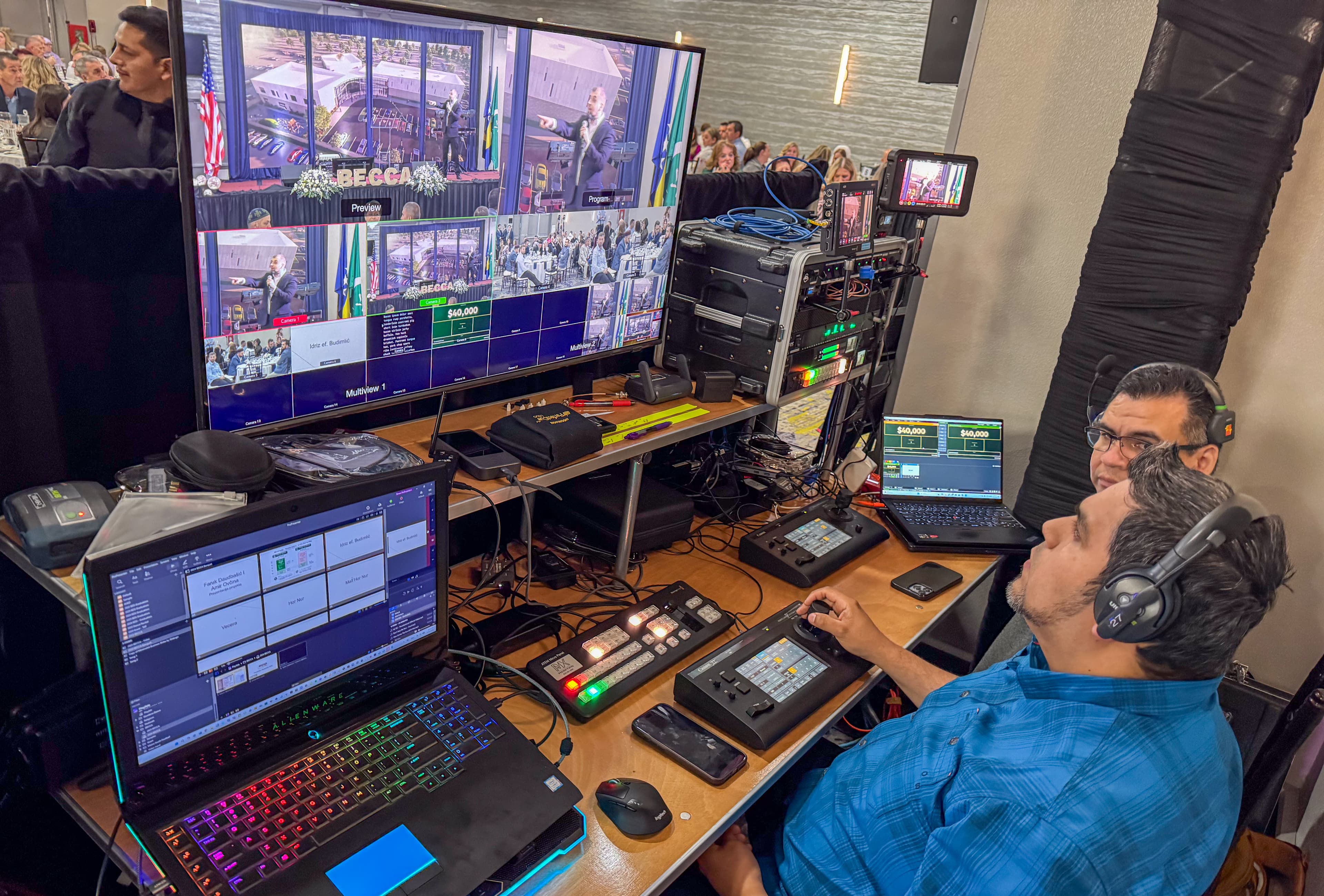 Two technicians operate a live video production station with multiple monitors and control panels.