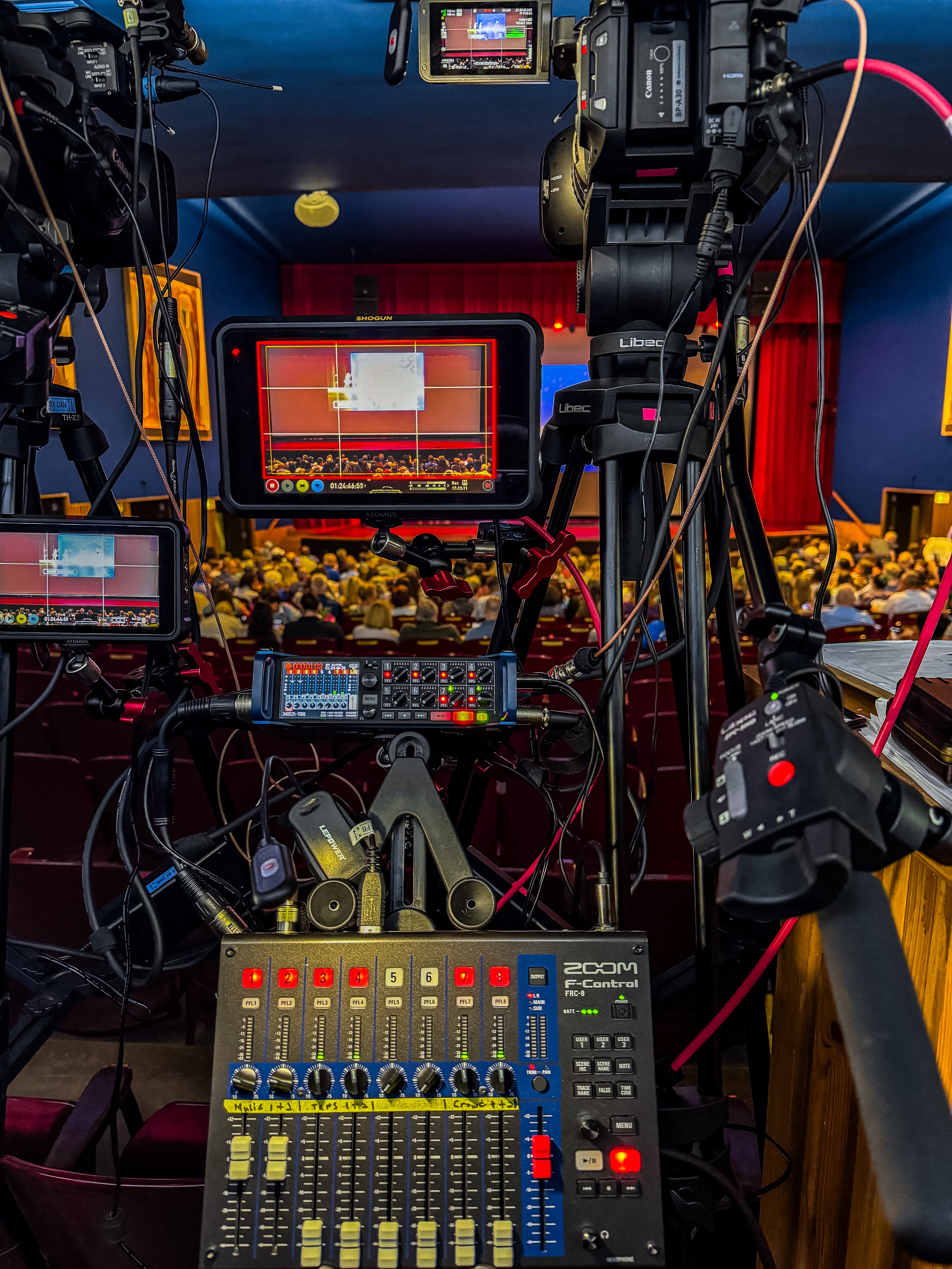 Professional video cameras and an audio mixer capturing a live stage performance in a theater.