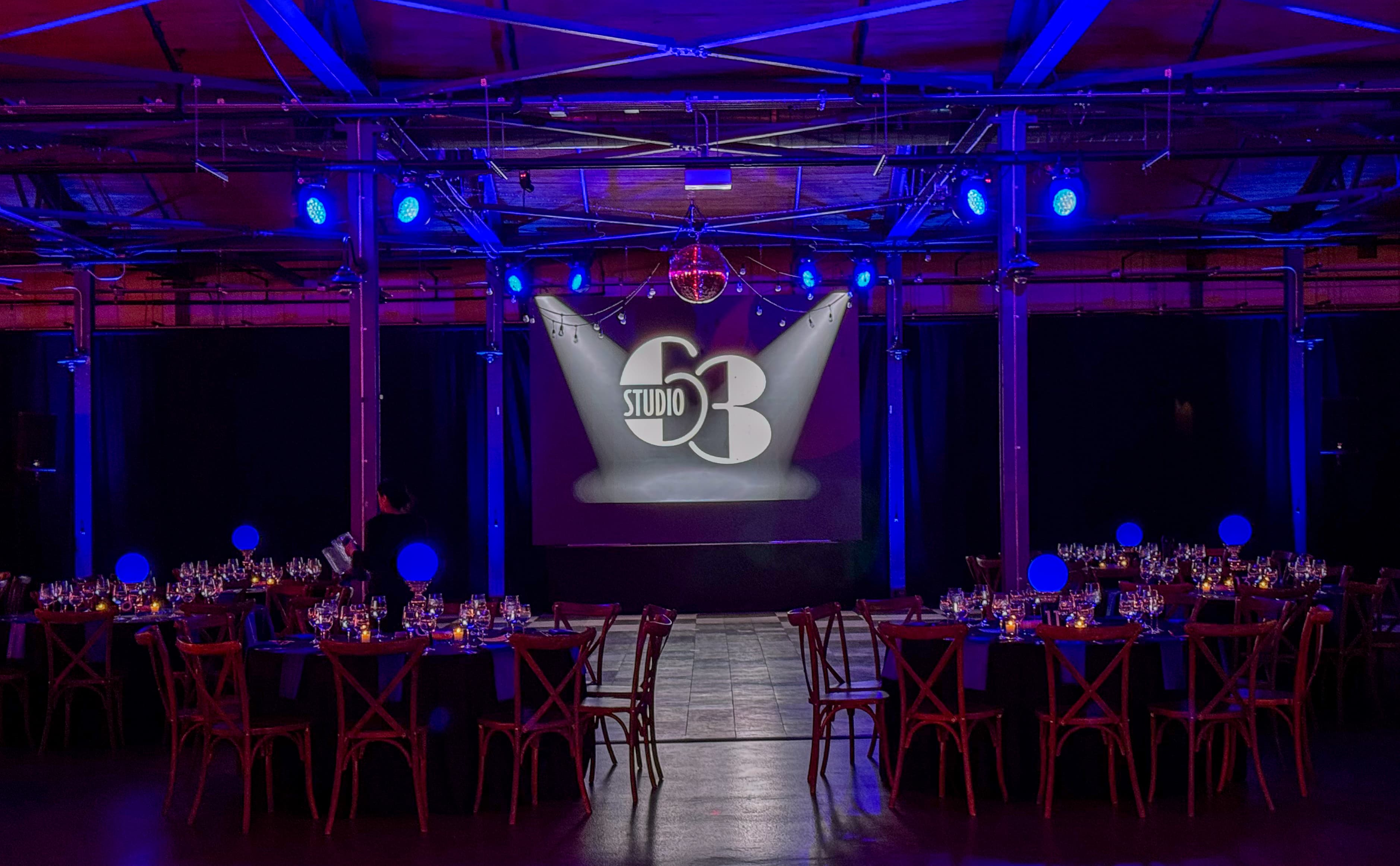 Elegant event space with blue lighting, set tables, and a Studio 53 logo screen.